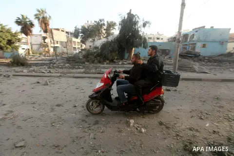 Palestinians ride their motorcycle and pass in front of the remains of a destroyed police station after Israeli air strike in al-Shijaia in the east of Gaza city on, 19 November 2012. The Palestinian civilian death toll...