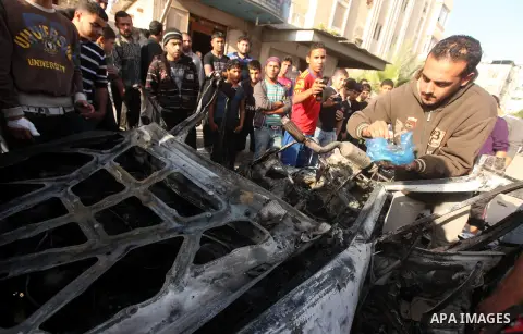 Palestinians gather around a destroyed car which targeted by Israeli airstrike in the northen Gaza city, 19 November, 2012. Israeli aircraft killed A Palestinian and wounded two others in the raid. Media reports that Isr...
