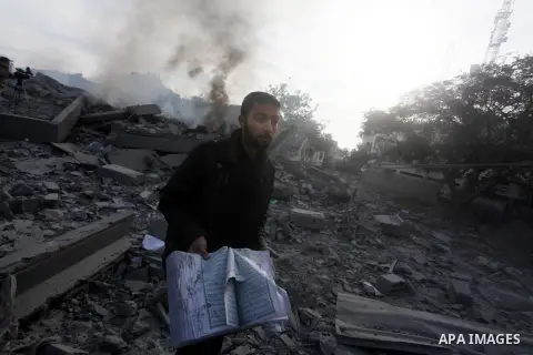 A Palestinian man carry a copy of the holy Quraan at government offices destroyed in an Israeli airstrike in Gaza City, 21 November 2012. Palestinian militants renewed their rocket fire on Israel 21 November and Israel c...