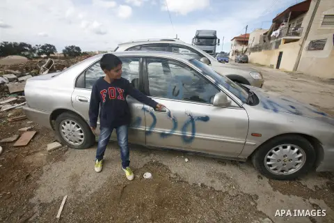 A Palestinian boy stands next to a car with a graffiti reading in Hebrew "Gaza: the price to pay" in the Palestinian neighborhood of Shuafat in Israeli annexed East Jerusalem, , on November 25, 2012. Unknown assailants v...