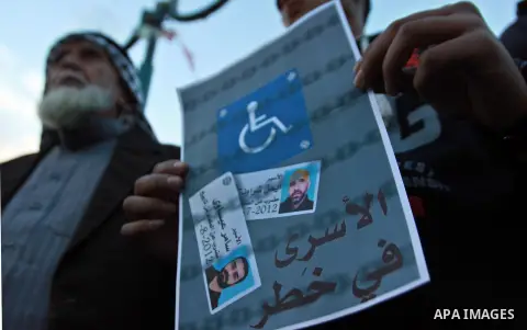 Palestinians hold a poster of Palestinian prisoners during a protest calling for the release them from Israeli jails and in support of prisoners on hunger strike, in the West Bank city of Nablus on 26 November 2012. Phot...