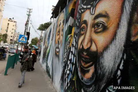 Palestinians walk in front of a mural of late Palestinian leader Yasser Arafat in Gaza City on November 27, 2012. The body of Arafat was exhumed, eight years after his death, as part of an investigation into allegations...