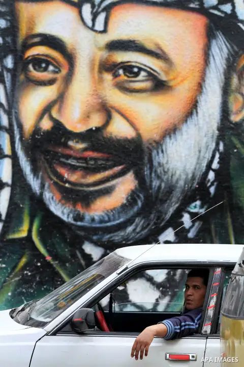 Palestinians walk in front of a mural of late Palestinian leader Yasser Arafat in Gaza City on November 27, 2012. The body of Arafat was exhumed, eight years after his death, as part of an investigation into allegations...