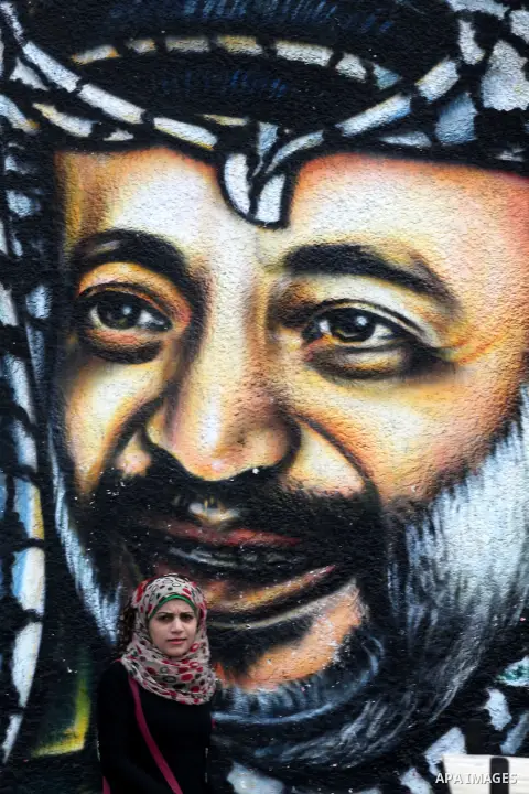 Palestinians walk in front of a mural of late Palestinian leader Yasser Arafat in Gaza City on November 27, 2012. The body of Arafat was exhumed, eight years after his death, as part of an investigation into allegations...
