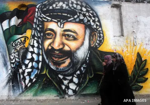Palestinians walk in front of a mural of late Palestinian leader Yasser Arafat in Gaza City on November 27, 2012. The body of Arafat was exhumed, eight years after his death, as part of an investigation into allegations...