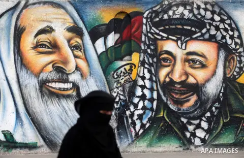 Palestinians walk in front of a mural of late Palestinian leader Yasser Arafat in Gaza City on November 27, 2012. The body of Arafat was exhumed, eight years after his death, as part of an investigation into allegations...