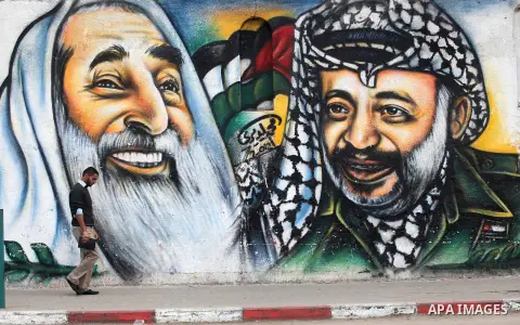 Palestinians walk in front of a mural of late Palestinian leader Yasser Arafat in Gaza City on November 27, 2012. The body of Arafat was exhumed, eight years after his death, as part of an investigation into allegations...