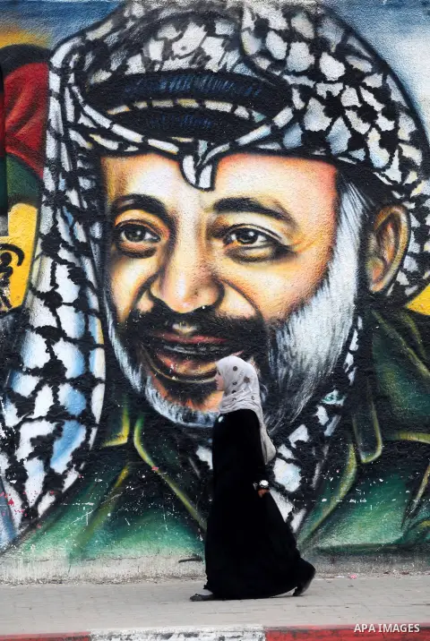 Palestinians walk in front of a mural of late Palestinian leader Yasser Arafat in Gaza City on November 27, 2012. The body of Arafat was exhumed, eight years after his death, as part of an investigation into allegations...