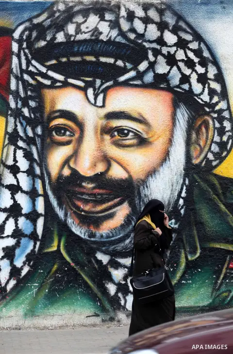 Palestinians walk in front of a mural of late Palestinian leader Yasser Arafat in Gaza City on November 27, 2012. The body of Arafat was exhumed, eight years after his death, as part of an investigation into allegations...