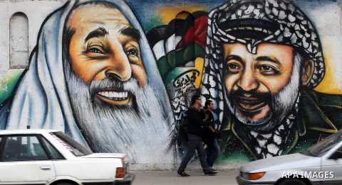 Palestinians walk in front of a mural of late Palestinian leader Yasser Arafat in Gaza City on November 27, 2012. The body of Arafat was exhumed, eight years after his death, as part of an investigation into allegations...