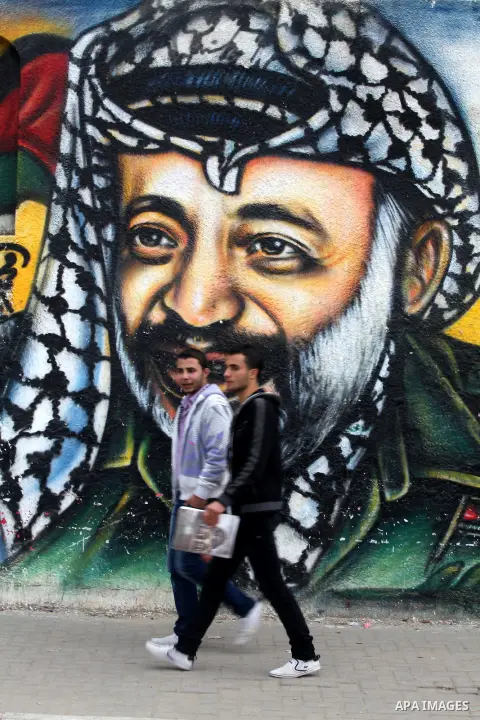 Palestinians walk in front of a mural of late Palestinian leader Yasser Arafat in Gaza City on November 27, 2012. The body of Arafat was exhumed, eight years after his death, as part of an investigation into allegations...