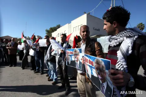 Palestinians hold national flags and a poster of Canadian Prime Minister Stephen Harper superimposed with a face of a dog during a protest following his remarks about the Palestinian UN bid for an observer state status,...