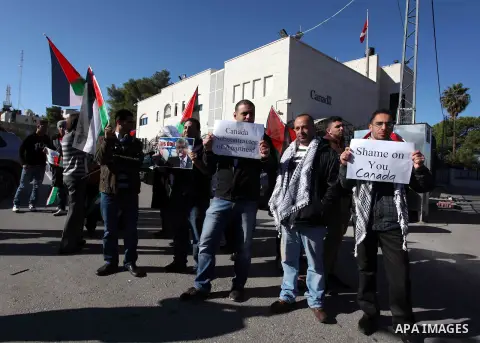Palestinians hold national flags and a poster of Canadian Prime Minister Stephen Harper superimposed with a face of a dog during a protest following his remarks about the Palestinian UN bid for an observer state status,...