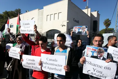 Palestinians hold national flags and a poster of Canadian Prime Minister Stephen Harper superimposed with a face of a dog during a protest following his remarks about the Palestinian UN bid for an observer state status,...