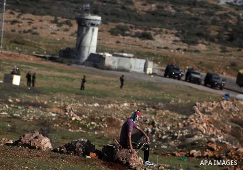 A Palestinian protester hurls a stone at Israeli security forces during a protest against the expansion of the nearby Jewish settlement of Halamish, in the West Bank village of Nabi Saleh near Ramallah, Friday, Nov. 30,...