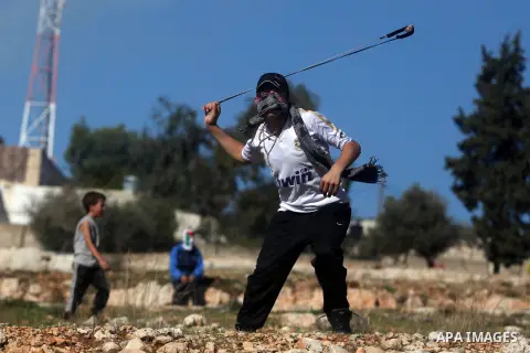 A Palestinian protester hurls a stone at Israeli security forces during a protest against the expansion of the nearby Jewish settlement of Halamish, in the West Bank village of Nabi Saleh near Ramallah, Friday, Nov. 30,...