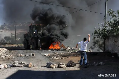 A Palestinian protester throws stones at Israeli bulldozer on the sidelines of a demonstration against the expropriations by Israel in the West Bank village of Kafr Qaddum, near Nablus, on November 30, 2012. Photo by Ned...