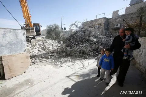 A Palestinian man walks with his family as an Israeli bulldozer destroys a home in East Jerusalem district of Sur Baher on December 1, 2012 after an Israeli court ruled that the house was built without a municipality per...