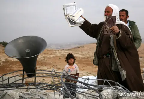 A Palestinian man holds copies of the Koran as he stands near the speaker of a mosque that was demolished by Israeli forces in the West Bank village of al-Mufaqara, south of Hebron, on December 04, 2012. Photo by Mamoun...