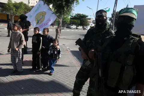 Palestinian children walk pass members of the Ezzedine al-Qassam brigade, the armed wing Hamas, as they prepare for the arrival of the Islamist movement's exiled politburo chief Khaled Meshaal who is due in the Gaza Stri...