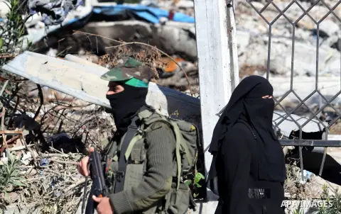 A Palestinian woman walk pass a member of the Ezzedine al-Qassam brigade, the armed wing Hamas, as they prepare for the arrival of the Islamist movement's exiled politburo chief Khaled Meshaal who is due in the Gaza Stri...