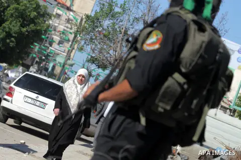Palestinians walk pass members of the Ezzedine al-Qassam brigade, the armed wing Hamas, as they prepare for the arrival of the Islamist movement's exiled politburo chief Khaled Meshaal who is due in the Gaza Strip to cel...