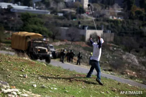 A Palestinian protester uses a slingshot to throw stones from the roof of a house during clashes following a demonstration against the expropriation of Palestinian land by Israel in the West Bank village of Nabi Saleh on...