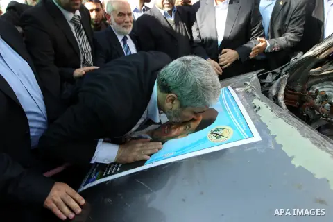 Hamas leader Khaled Meshaal kisses a poster depicting late Hamas military commander Ahmed Al-Jaabari pasted on the remains of the car that he was riding in when he was killed in an Israeli air strike, at Rafah Crossing,...
