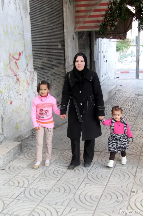 A Palestinian woman, Samar Bulbul walks with her family at a street in Gaza city on Dec. 18,2012. Bulbul lost hearing after an Israeli airstrike targeted two Palestinian militants' car in Gaza city in December 2011. Phot...