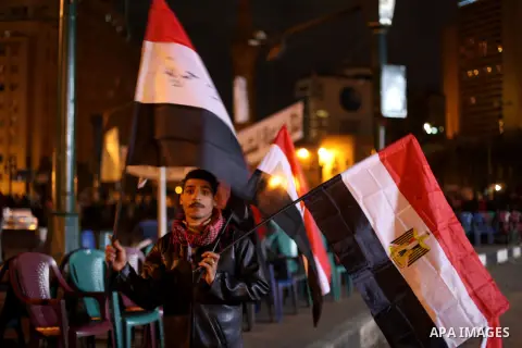 An Egyptian man hold national flags as others gather at Tahrir square in Cairo, Egypt, Friday, Dec. 21, 2012. Running clashes between rival protesters erupted in Egypt's second city Alexandria, on the eve of the final ro...