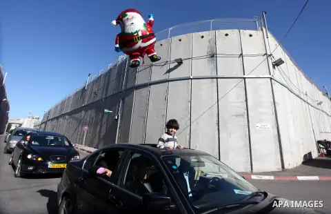 A Palestinian boy holds a Santa Claus balloon as a convey of cars transporting the Latin Patriarch of Jerusalem Fouad Twal cross through an Israeli checkpoint to the West Bank city of Bethlehem December 24, 2012. Twal cr...