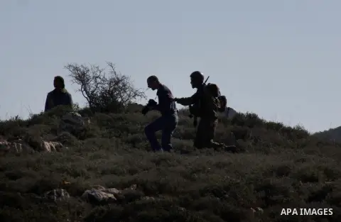 An Israeli soldier stops a settler from he Yetshar settlement after settlers attacked Palestinian farmers from the West Bank village of Qusra near the West Bank City of Nablus 27 December 2012. Photo by Nedal Eshtayah