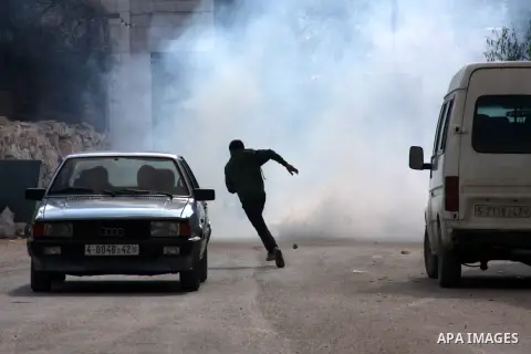 A Palestinian man runs cover from tear gas during a search carried out by Israeli soldiers after they raided the village of Urif, near Nablus, West Bank, 27 December 2012. Israeli soldiers raided the village after clashe...