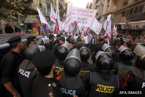 protesters holding signs, in front of police officers near the Shura Council, the upper house of parliament where the Constituent Assembly drafted the country's new constitution, as protesters against Egypt's President M...