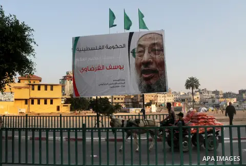 Palestinians ride their donkey cart past a banner with picture of prominent Muslim scholar Sheikh Yusuf al-Qaradawi, in Gaza city on May 07, 2013. Al-Qaradawi, Qatar-based cleric who is widely-respected through the Musli...