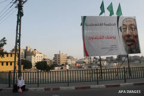 A Palestinian woman sits next to a banner with picture of prominent Muslim scholar Sheikh Yusuf al-Qaradawi, in Gaza city on May 07, 2013. Al-Qaradawi, Qatar-based cleric who is widely-respected through the Muslim world,...