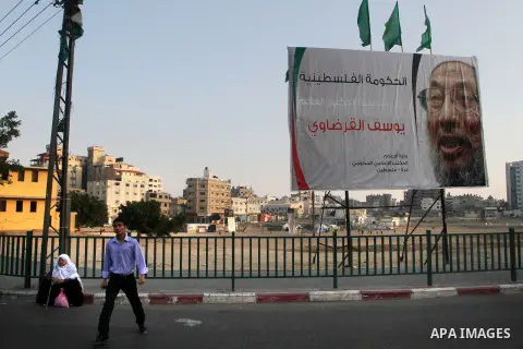 A Palestinian man walks past a banner with picture of prominent Muslim scholar Sheikh Yusuf al-Qaradawi, in Gaza city on May 07, 2013. Al-Qaradawi, Qatar-based cleric who is widely-respected through the Muslim world, and...