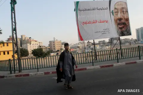 A Palestinian man walks past a banner with picture of prominent Muslim scholar Sheikh Yusuf al-Qaradawi, in Gaza city on May 07, 2013. Al-Qaradawi, Qatar-based cleric who is widely-respected through the Muslim world, and...