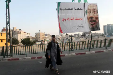A Palestinian man walks past a banner with picture of prominent Muslim scholar Sheikh Yusuf al-Qaradawi, in Gaza city on May 07, 2013. Al-Qaradawi, Qatar-based cleric who is widely-respected through the Muslim world, and...