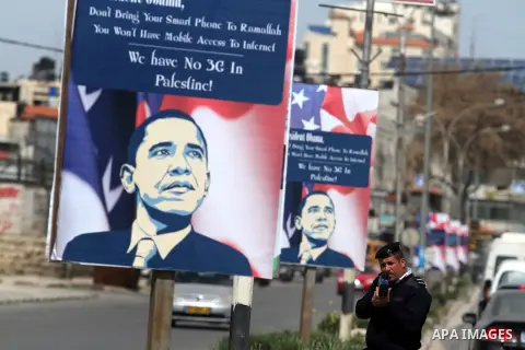 A Palestinian policeman stands next a poster with a slogan against the upcoming visit of US President Barack Obama to the West Bank city of Ramallah is seen on March 12, 2013, in central Ramallah. Obama's three-day visit...