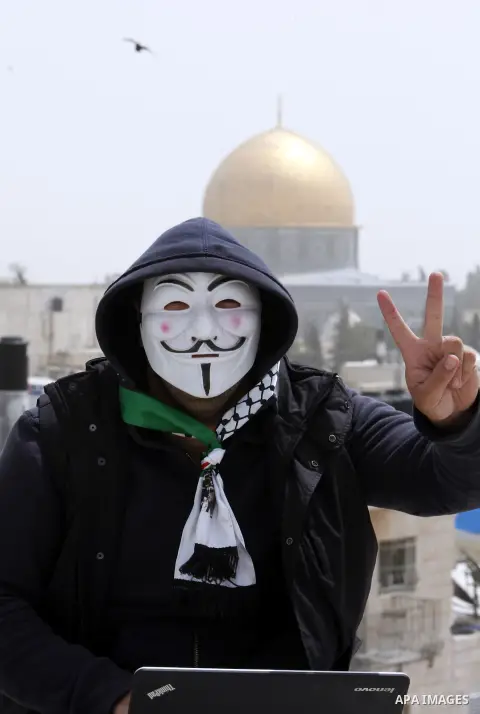 A Palestinian youth wearing masks used by computer hackers who attacked a number of Israeli websites recently, seen backdropped by the Dome of the Rock, in Jerusalem's Old City. April 09 2013. Photo by Sliman Khader