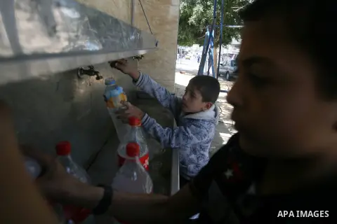 Palestinian children filling plastic bottles and jerry cans with drinking water from a public tap at the United Nations Relief and Works Agency (UNRWA) headquarters in the southern Gaza Strip refugee camp of Rafah on Apr...