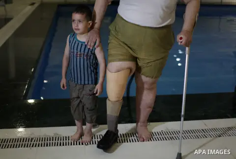 Palestinian Asad Redwan, 31, stands with his son after taking part in a swimming lesson inside al-Sadaka Club in Gaza City May 17, 2013. Al-Masri said that his leg was amputated after clashes between Palestinians and Isr...