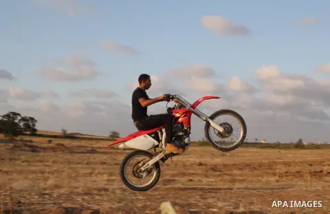 A Palestinian youth rides his motorcycle on sand dunes during the weekly sporting event in the town of Al-Zahra, in the southern Gaza City, on June 14, 2013. Palestinian youths use the dunes for riding their motorcycles,...