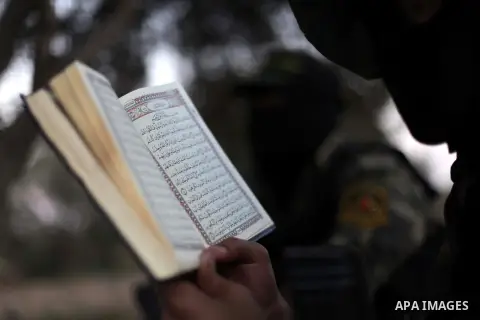 A Masked militant from al-Quds Brigades the armed wing of the Islamic Jihad organization, reads holy Quran during a guard the eastern border of Gaza City, on July 15, 2013. Photo by Ashraf Amra