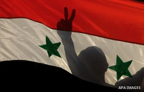 A Palestinian supporter of the Popular Front for the Liberation of Palestine (PFLP) marks a victory sign behind a Syrian flag as he protests in Rafah, in the southern Gaza Strip, on September 3, 2014, against US and Fren...