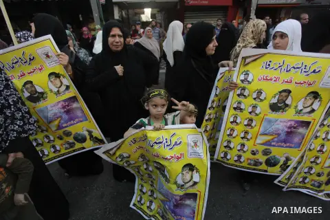 Palestinians hold placards as members of the Palestinian Islamic Jihad movement parade with guns on November 13, 2013 in the streets of Gaza City during an anti-Israel march as part of the celebrations marking the first...