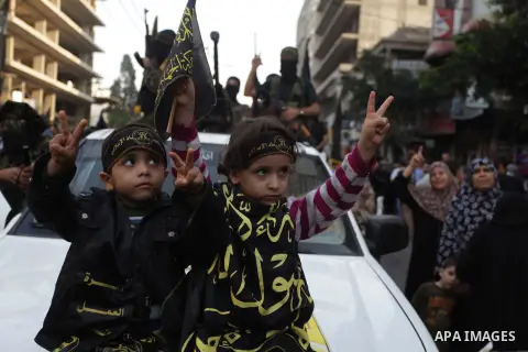 Palestinian children flash victory sign as members of the Palestinian Islamic Jihad movement parade with guns on November 13, 2013 in the streets of Gaza City during an anti-Israel march as part of the celebrations marki...