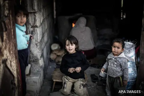 Palestinian children play as their mother bakes bread on firewood at her tin shack in Khan Younis refugee camp, in southern Gaza Strip, November 21, 2013. The UNRWA, which is facing a 36-million dollar deficit, halted 19...
