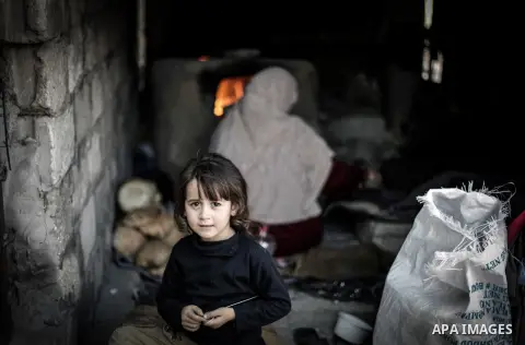 A Palestinian girl plays as her mother bakes bread on firewood at her tin shack in Khan Younis refugee camp, in southern Gaza Strip, November 21, 2013. The UNRWA, which is facing a 36-million dollar deficit, halted 19 ou...